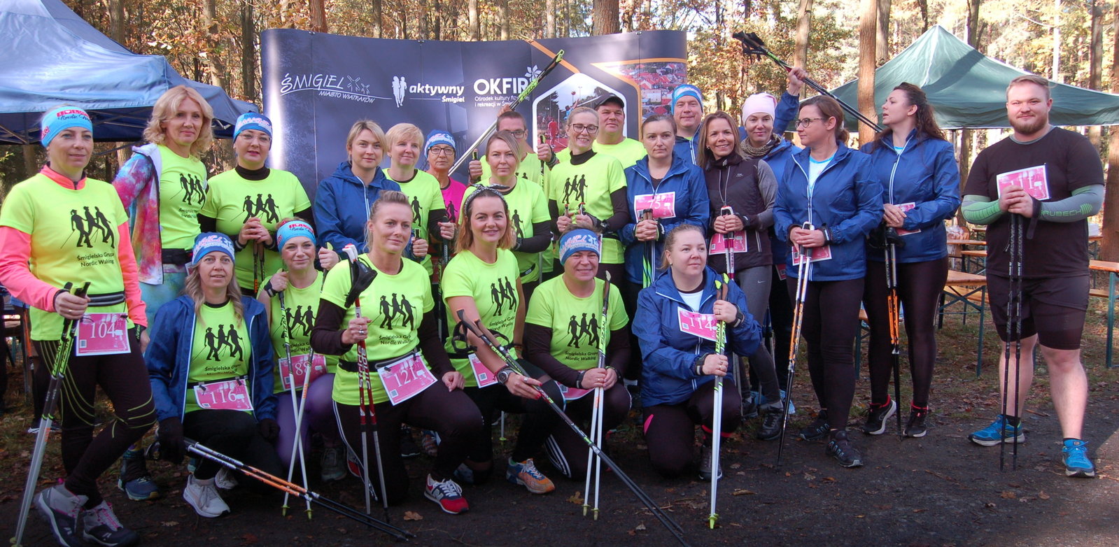 zdjęcie grupowe uczestników zawodów nordic walking. Część osób stoi, te z przodu klęczą