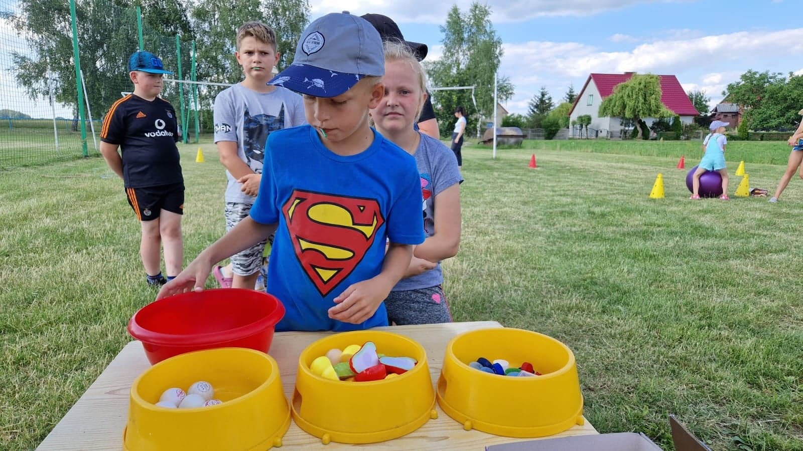chłopiec w niebieskiej koszulce ze znaczkiem supermena segreguje owoce plastikowe, nakrętki i piłeczki do ping ponga do żółtych 3 misek